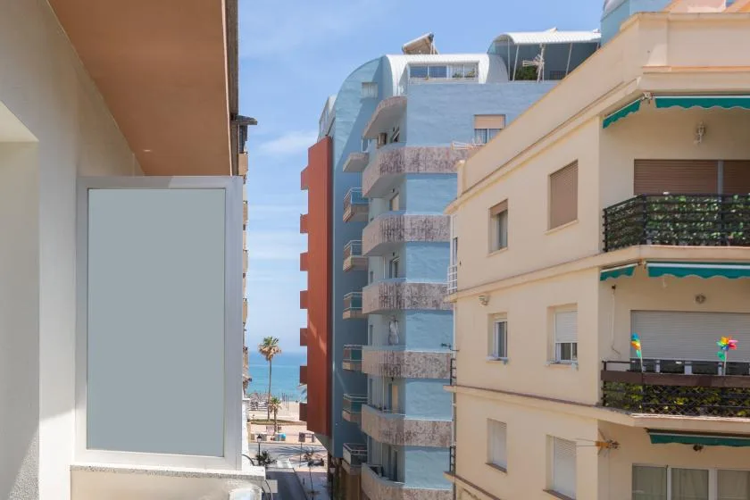 A view between apartment buildings reveals the sea in the distance.