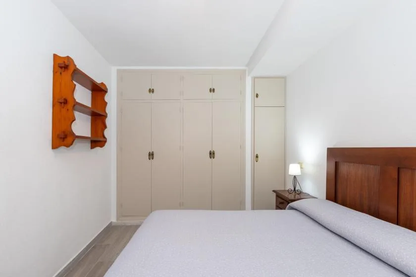 A bright bedroom with a bed, built-in cabinets, and a wooden wall shelf.