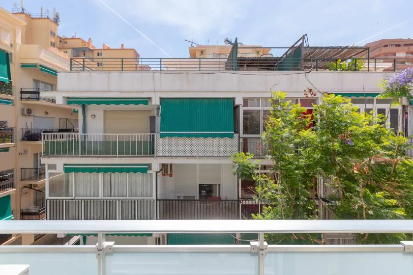 Apartment buildings with balconies and green awnings stand among leafy trees.