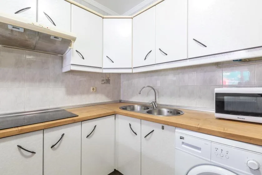 A compact kitchen with white cabinets, wooden counters, a sink, and a microwave.