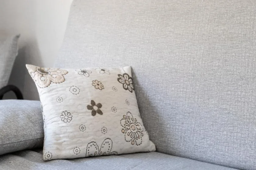 A light-colored sofa with a decorative floral cushion.