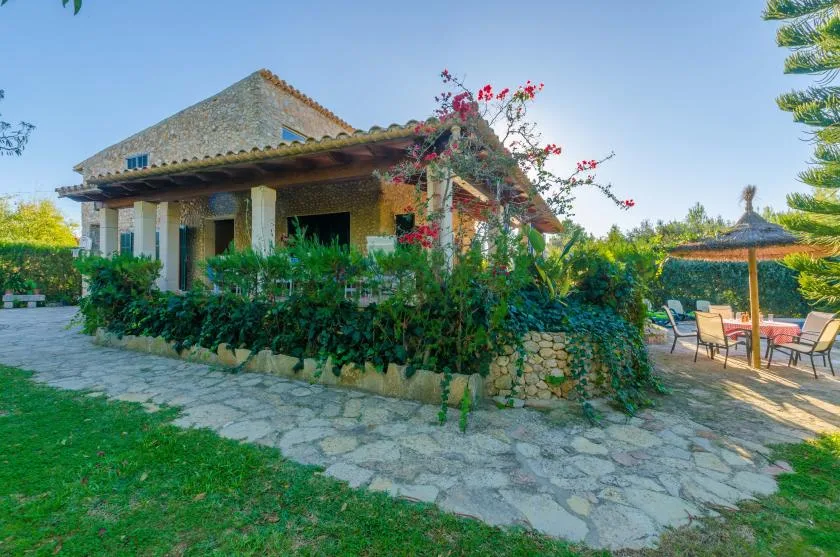 A stone-paved garden patio beside a low house, with outdoor seating under a shade canopy.