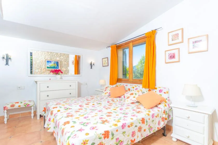 A bright bedroom with a floral bedspread and orange curtains.