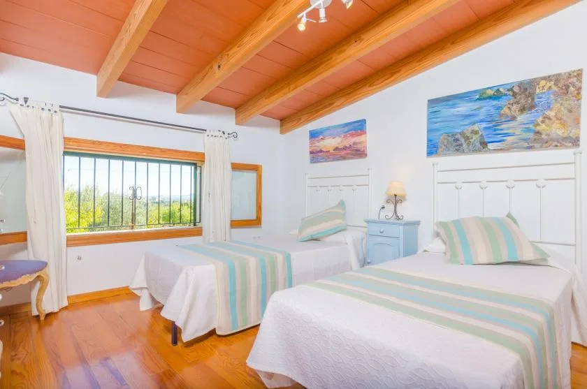 A bright bedroom with two beds, colorful striped bedding, and a large window.