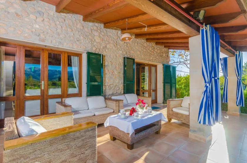 A covered stone patio with cushioned seating and blue-and-white curtains.