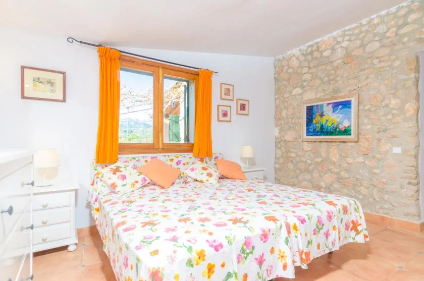 A bedroom with a floral bedspread and bright orange curtains.