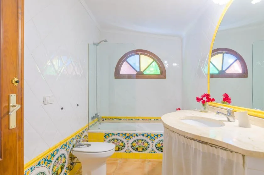 A tiled bathroom with a toilet, a curved sink counter, and an arched window.