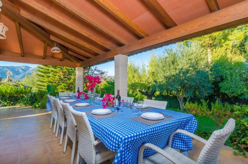 A covered outdoor dining area with a long table set beside a garden.