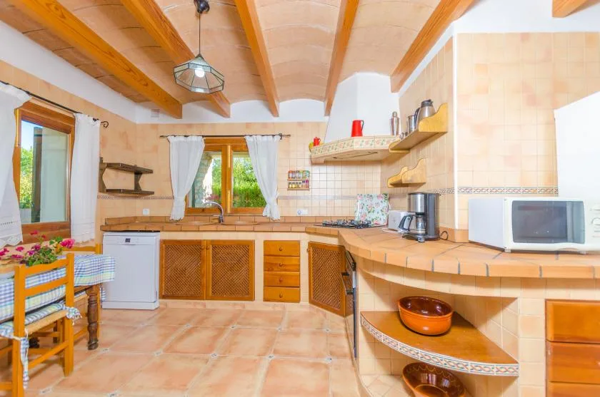 A tiled kitchen with wooden ceiling beams, a counter, and windows.