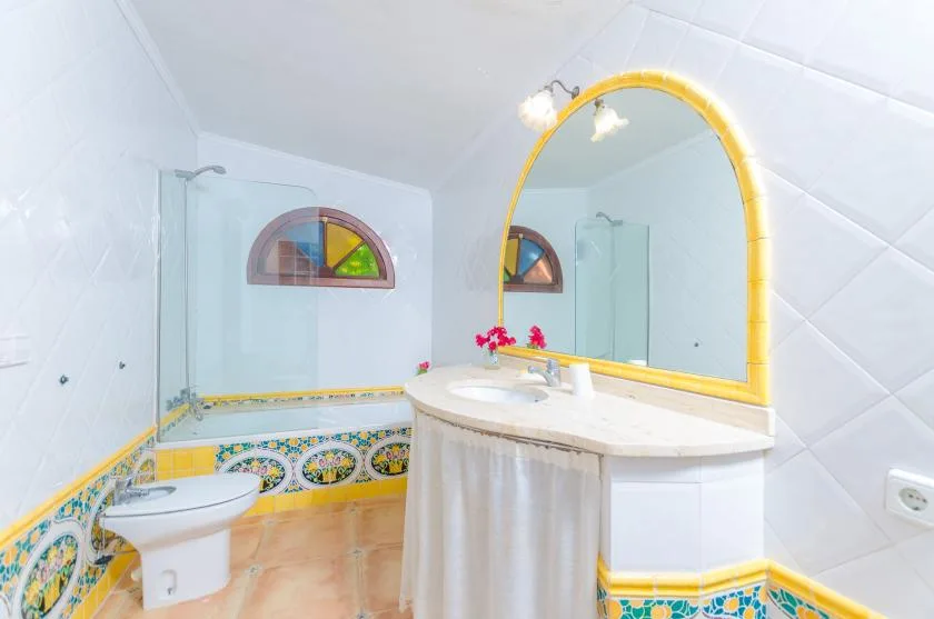 A bright bathroom with a bathtub, sink, and large arched mirror.