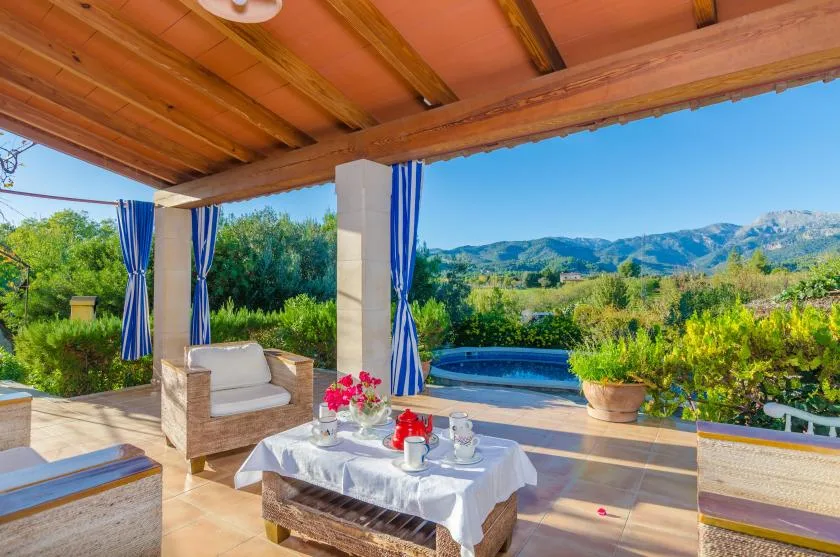 A covered outdoor patio with seating, a table, and a view of the hills.
