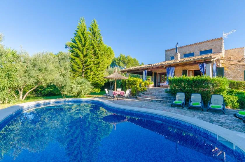 Outdoor swimming pool beside a stone house, with trees and seating around the patio.