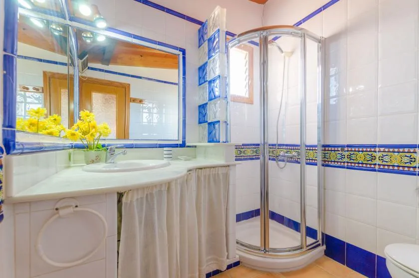 A tiled bathroom with a sink, large mirror, and curved glass shower enclosure.