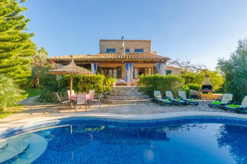 A swimming pool faces a garden patio and a stone house.