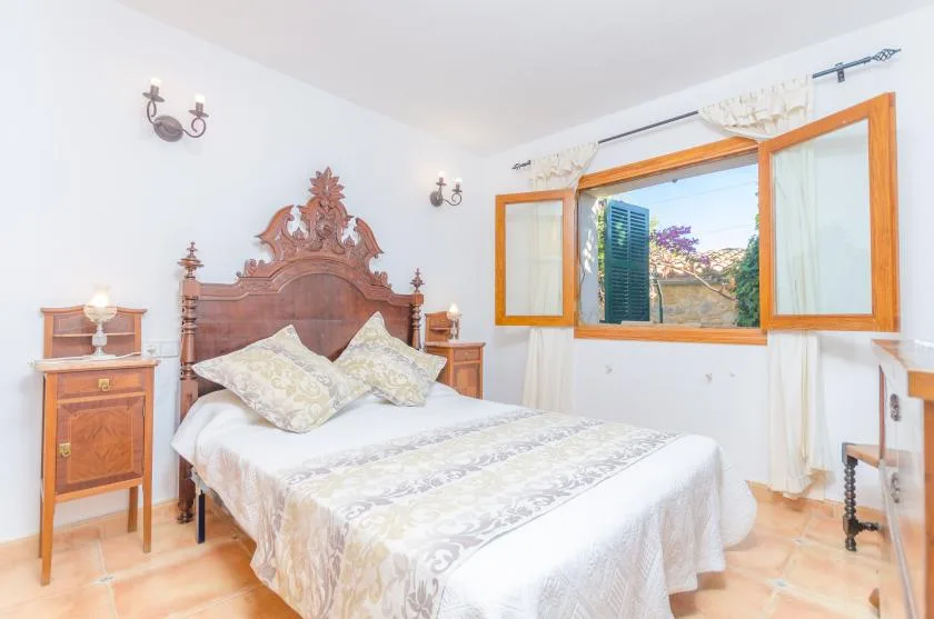 A bedroom with a carved wooden bed beneath an open window.