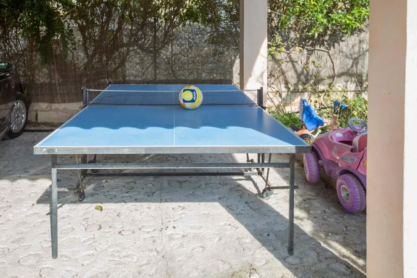 A blue ping-pong table stands in a sunlit outdoor courtyard.