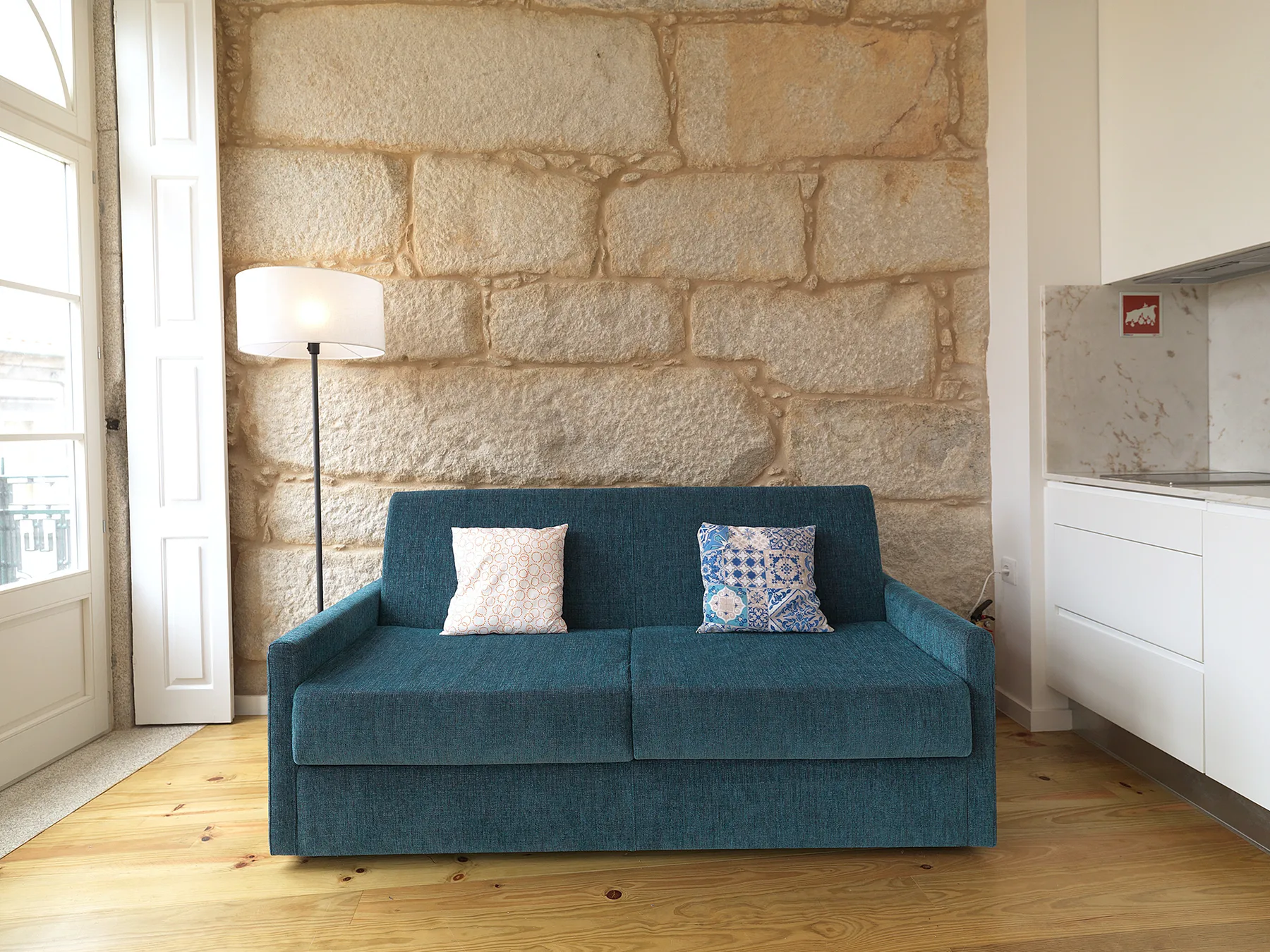 A studio living area with a teal sofa beside a stone wall.