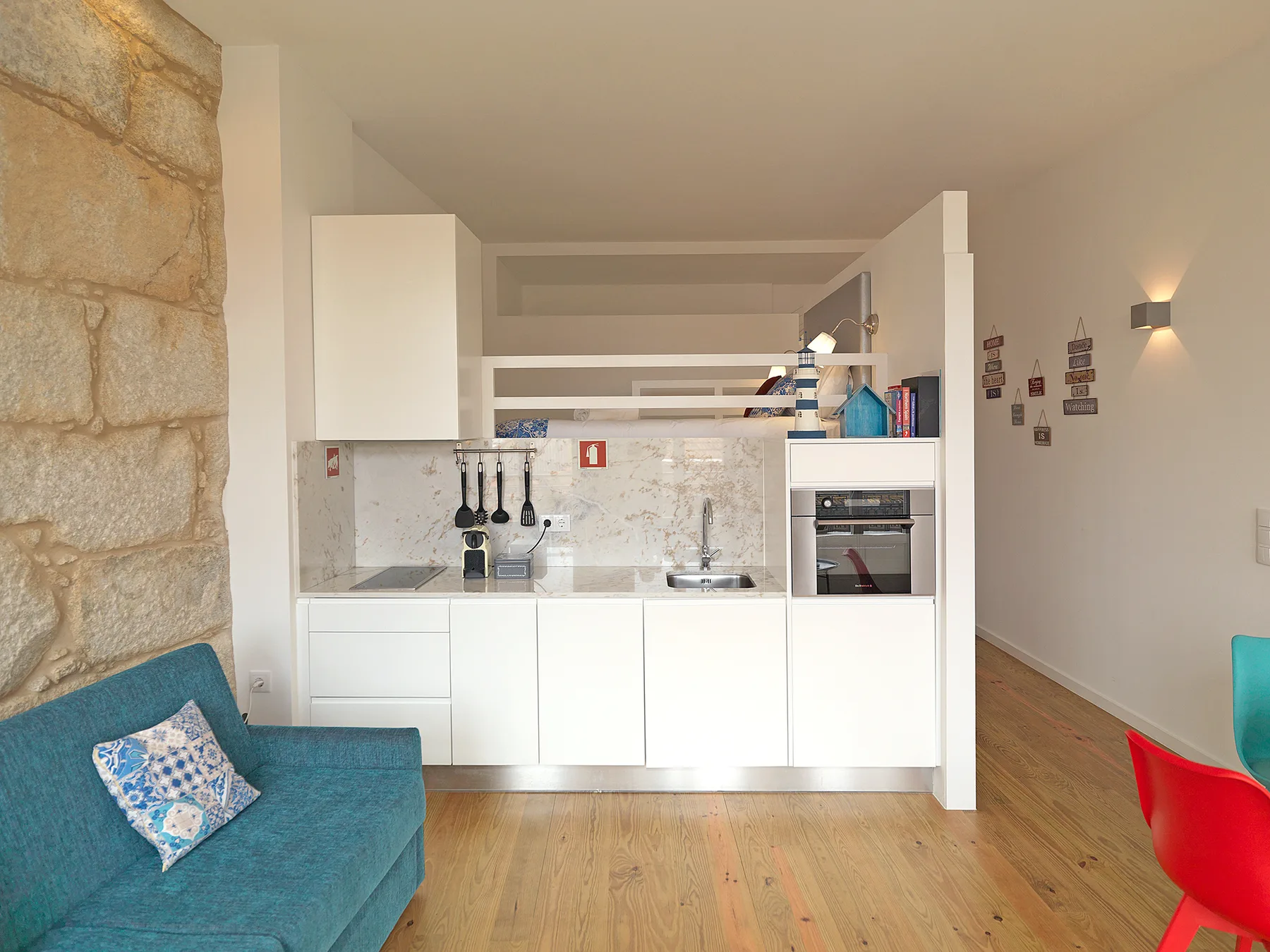 A studio living area with a compact kitchen, turquoise seating, and wooden flooring.