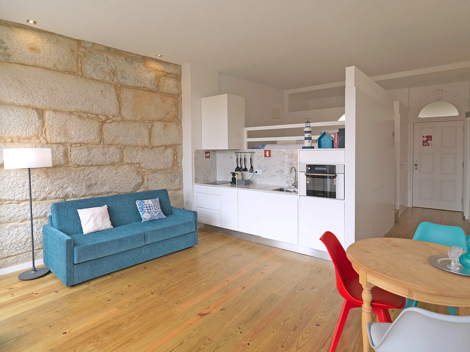 A studio living area with a teal sofa beside a compact kitchen.