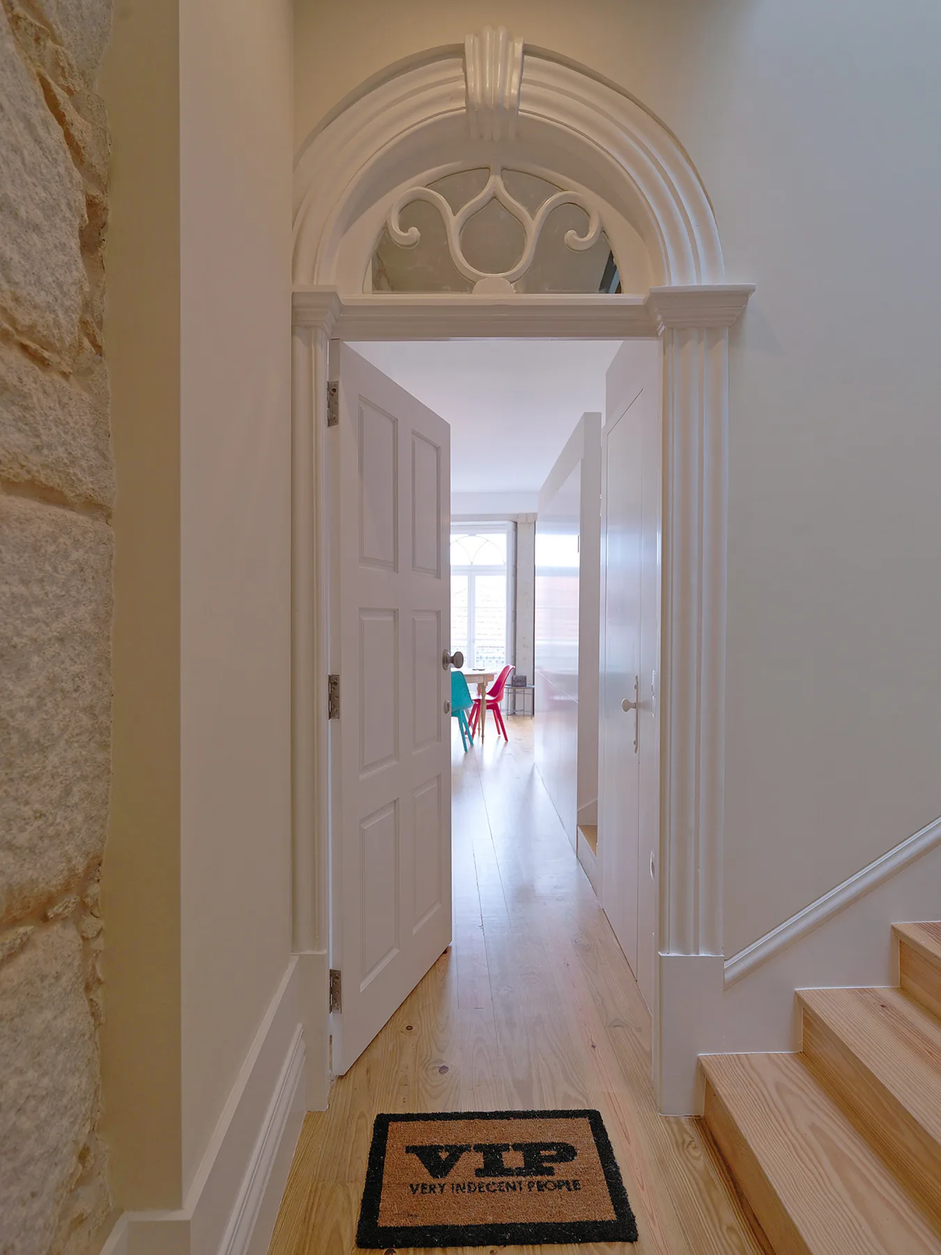 An open doorway leads to a bright room with a small table and red chairs.