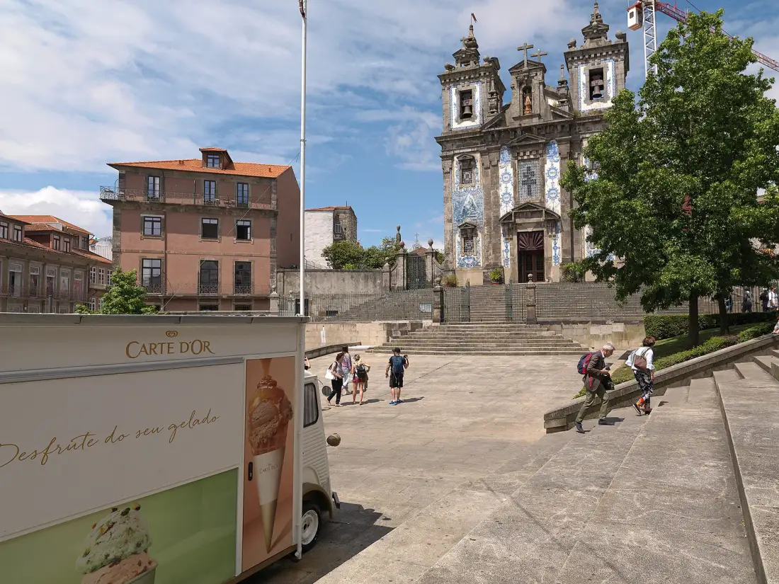 A stone church overlooks a broad paved square with steps and nearby buildings.