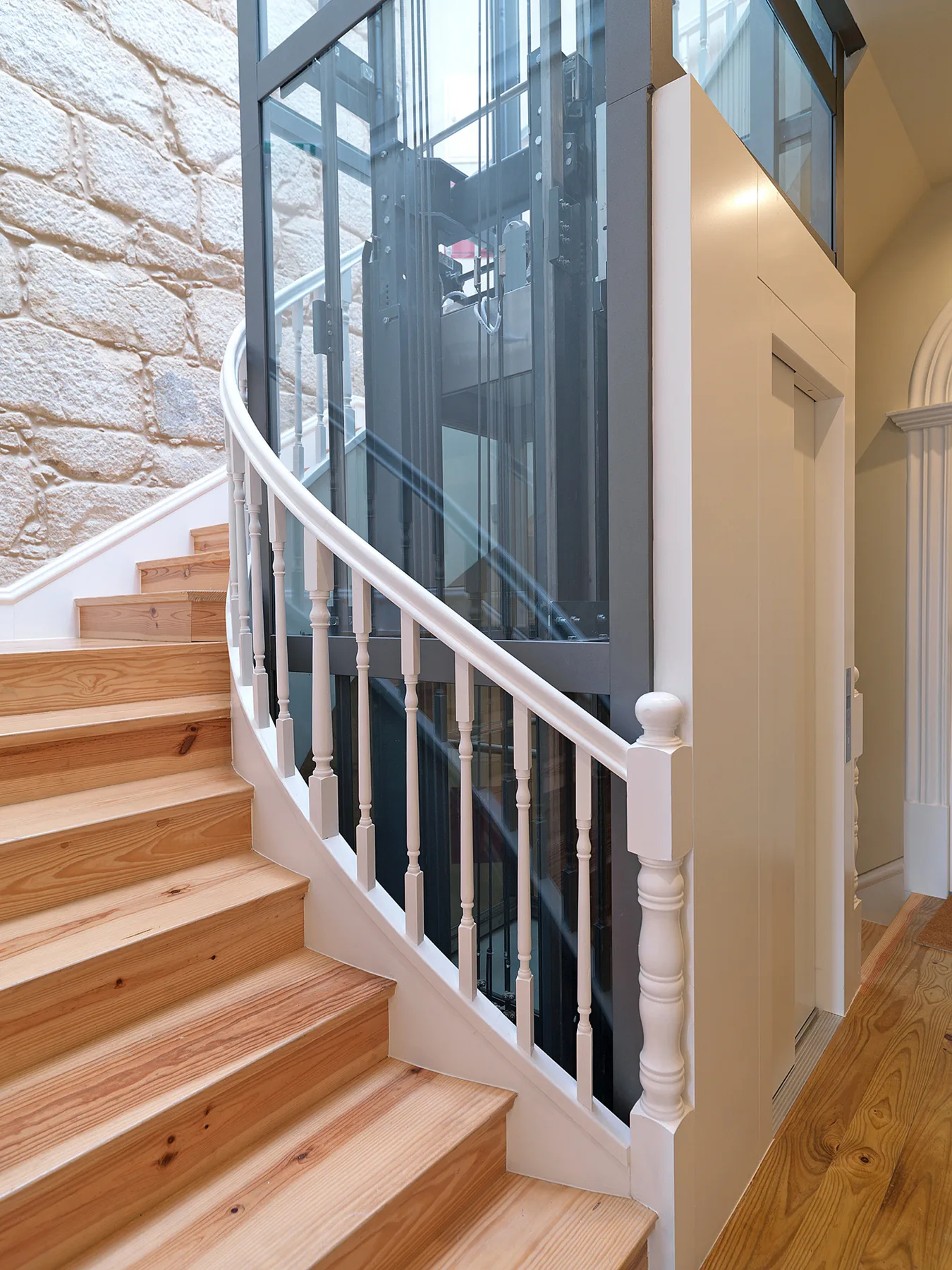 An interior staircase with wooden steps curves beside a glass elevator.
