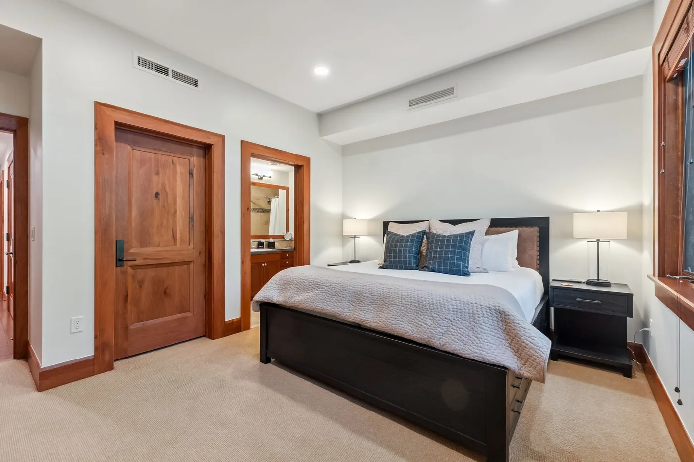 A bedroom with a neatly made bed, bedside tables, and wooden doors.