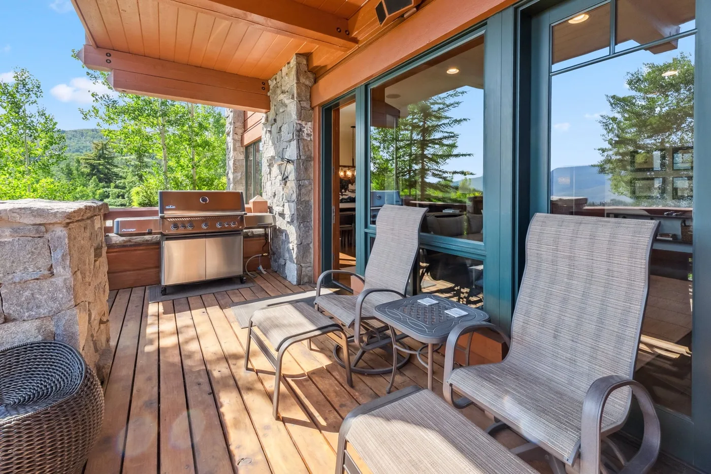 A covered outdoor deck has seating beside glass doors and a built-in grill.