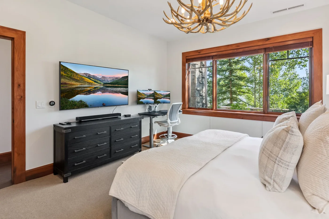 A bedroom with a bed, a desk, and a large window overlooking trees.
