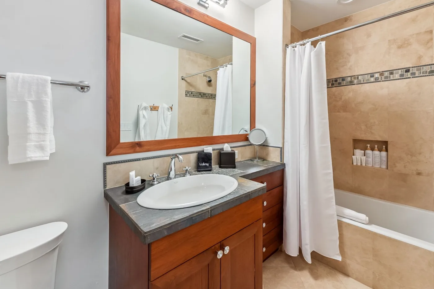A bathroom with a wooden vanity, sink, and curtained bathtub.