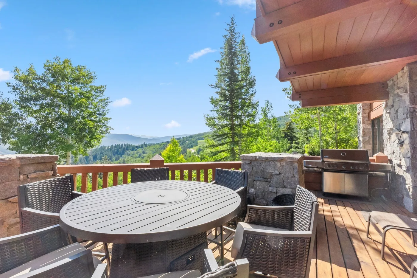 An outdoor dining area on a wooden deck overlooks a green, wooded landscape.
