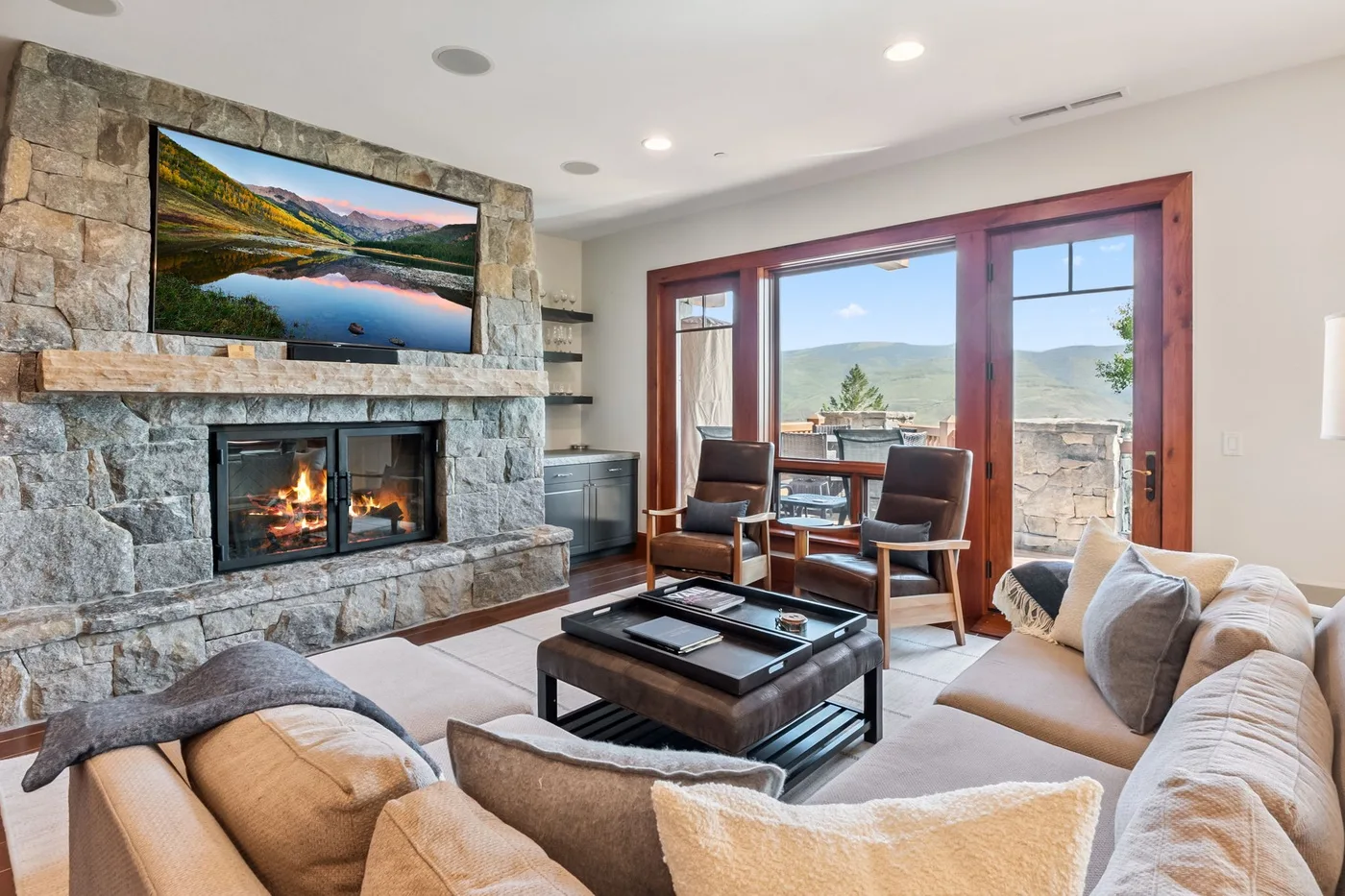 A living room with a stone fireplace, seating, and large windows overlooking a mountain view.