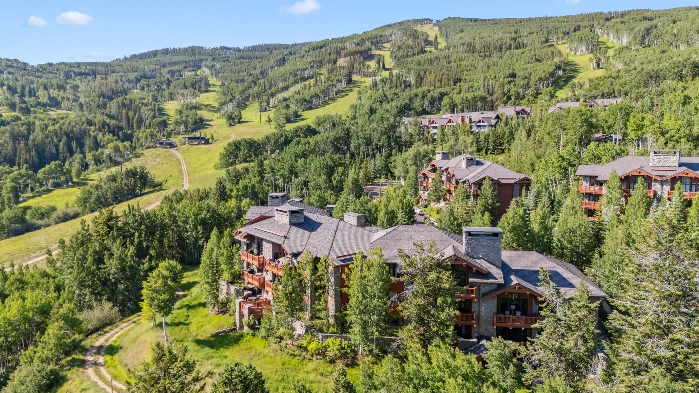 Mountain resort buildings sit among dense trees beneath a green hillside.