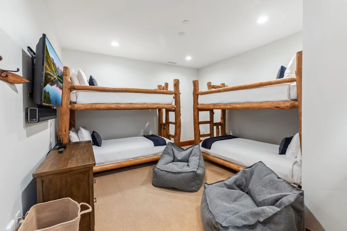 A bright bunk-bed room with gray floor cushions and a television on the wall.