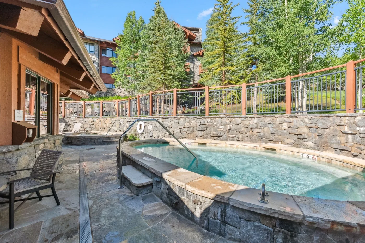 An outdoor pool with stone edging sits beside a paved patio and seating.