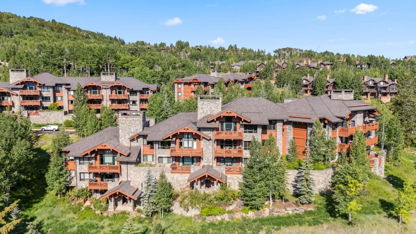 A hillside cluster of lodge buildings is surrounded by green trees.