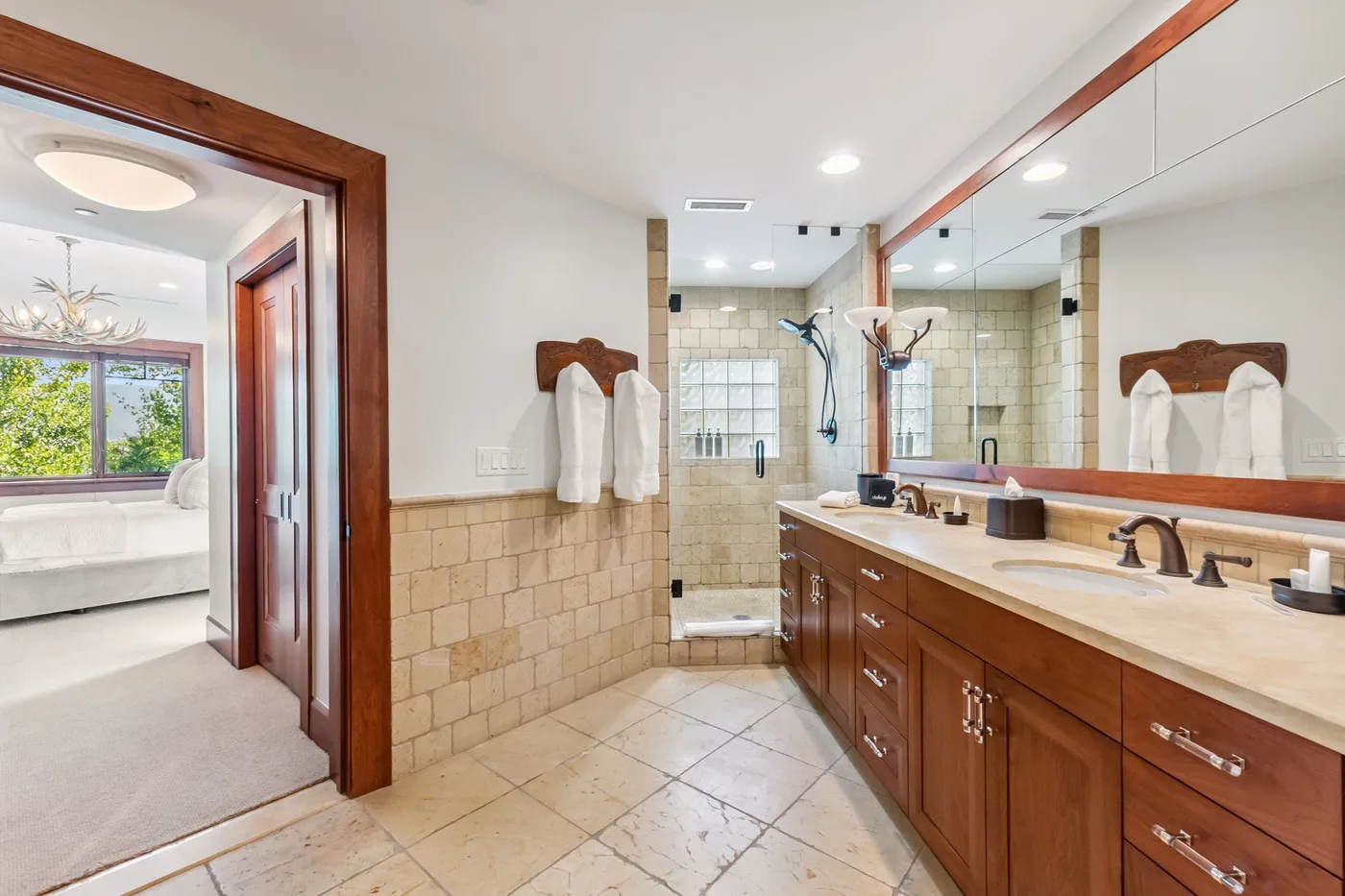 A bathroom with a long vanity and a glass shower beside an open doorway.