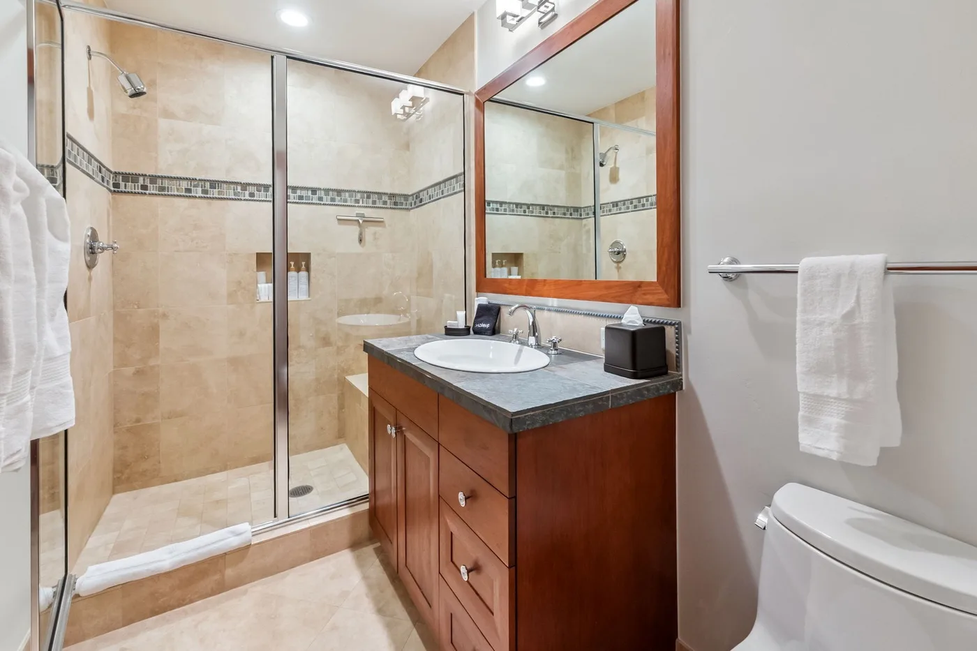 A bathroom with a glass shower, vanity, and toilet.