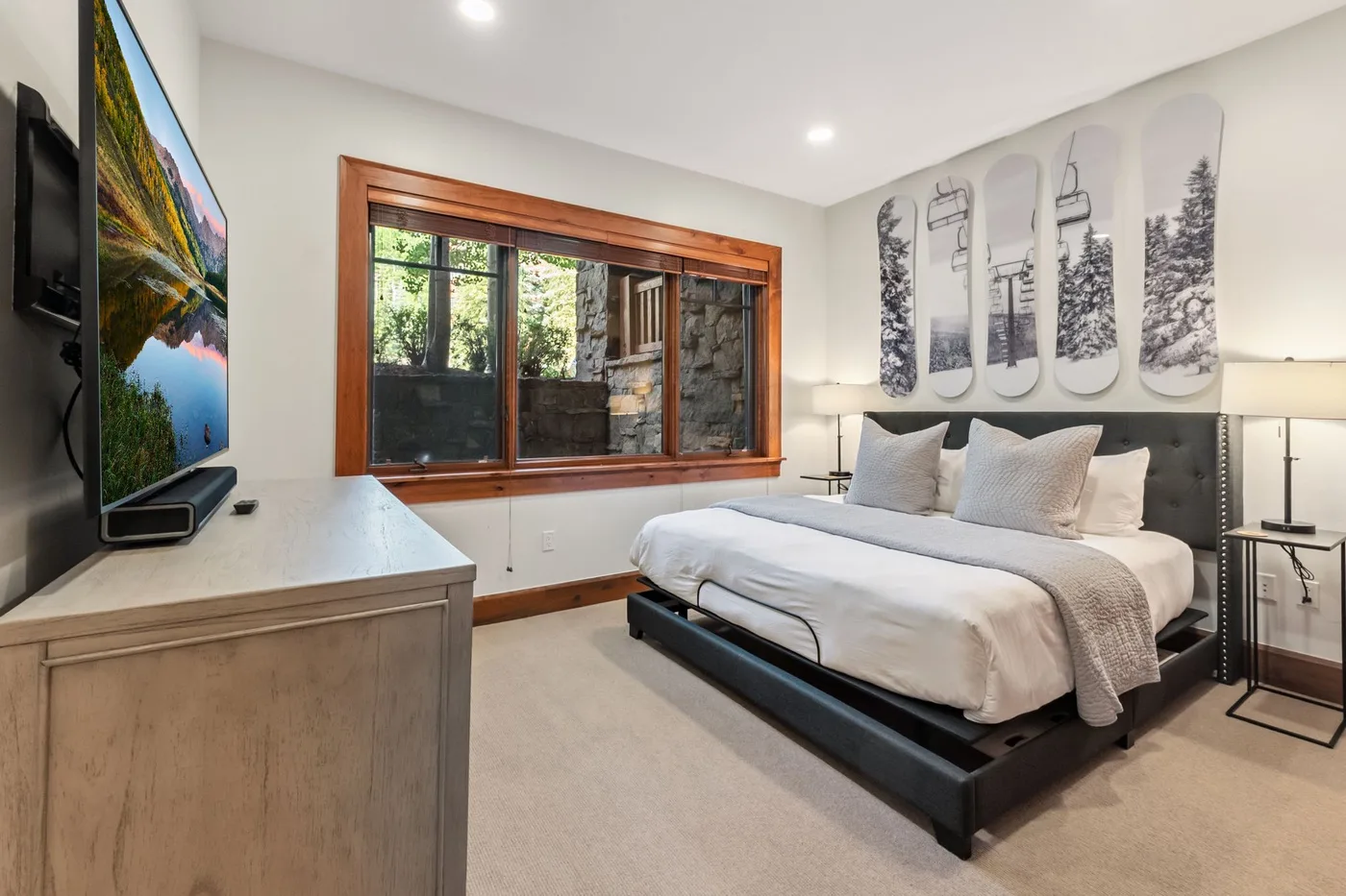 A bright bedroom with a bed, wall art, and a large window.