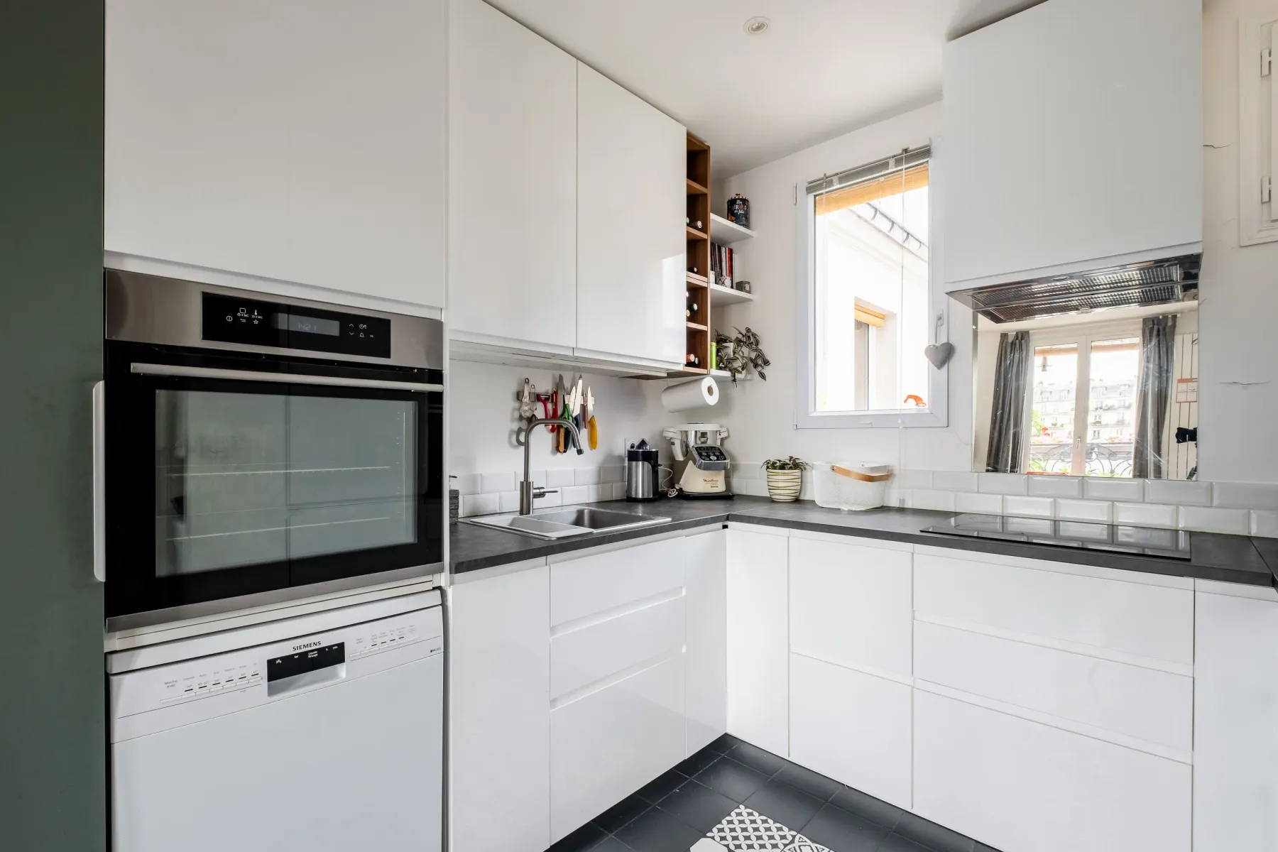 Una cocina blanca y luminosa con pequeños electrodomésticos y una ventana.