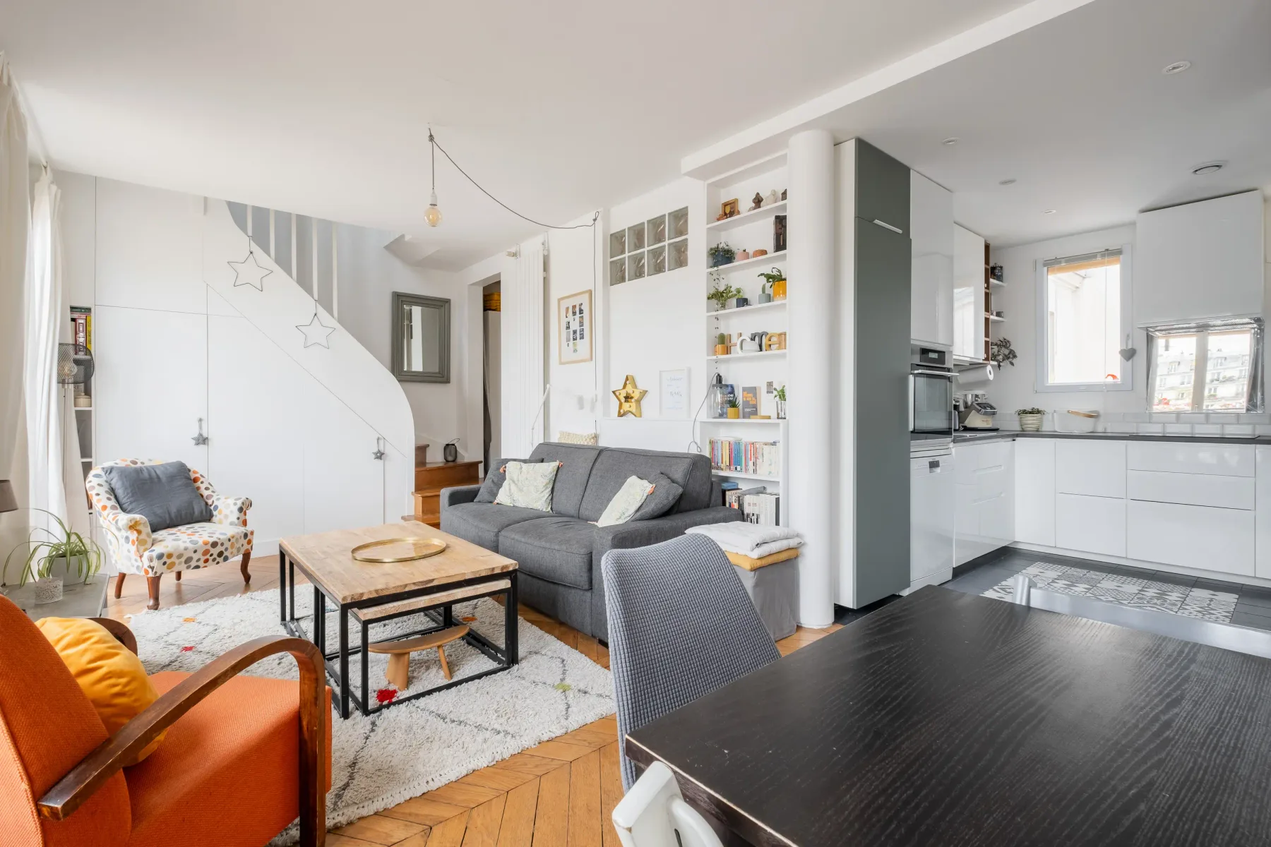 Una sala luminosa se abre a una cocina compacta, con asientos y estantes empotrados.