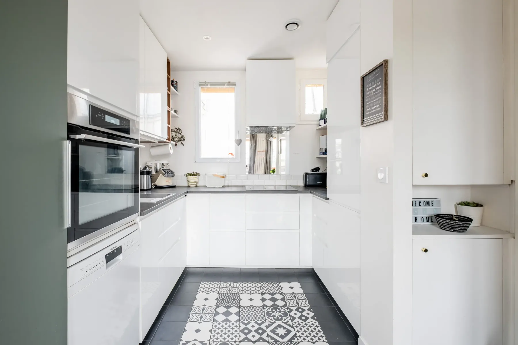 Cocina blanca y luminosa con electrodomésticos empotrados y una alfombra estampada.