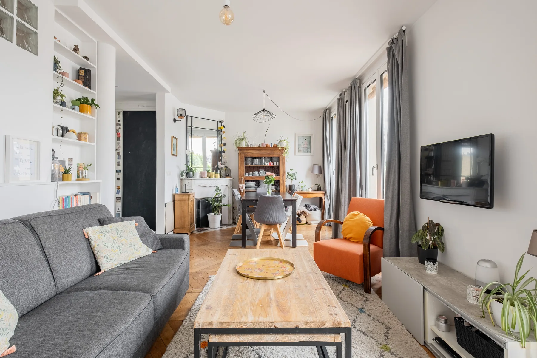 Una sala luminosa con asientos grises, un sillón naranja y un televisor.