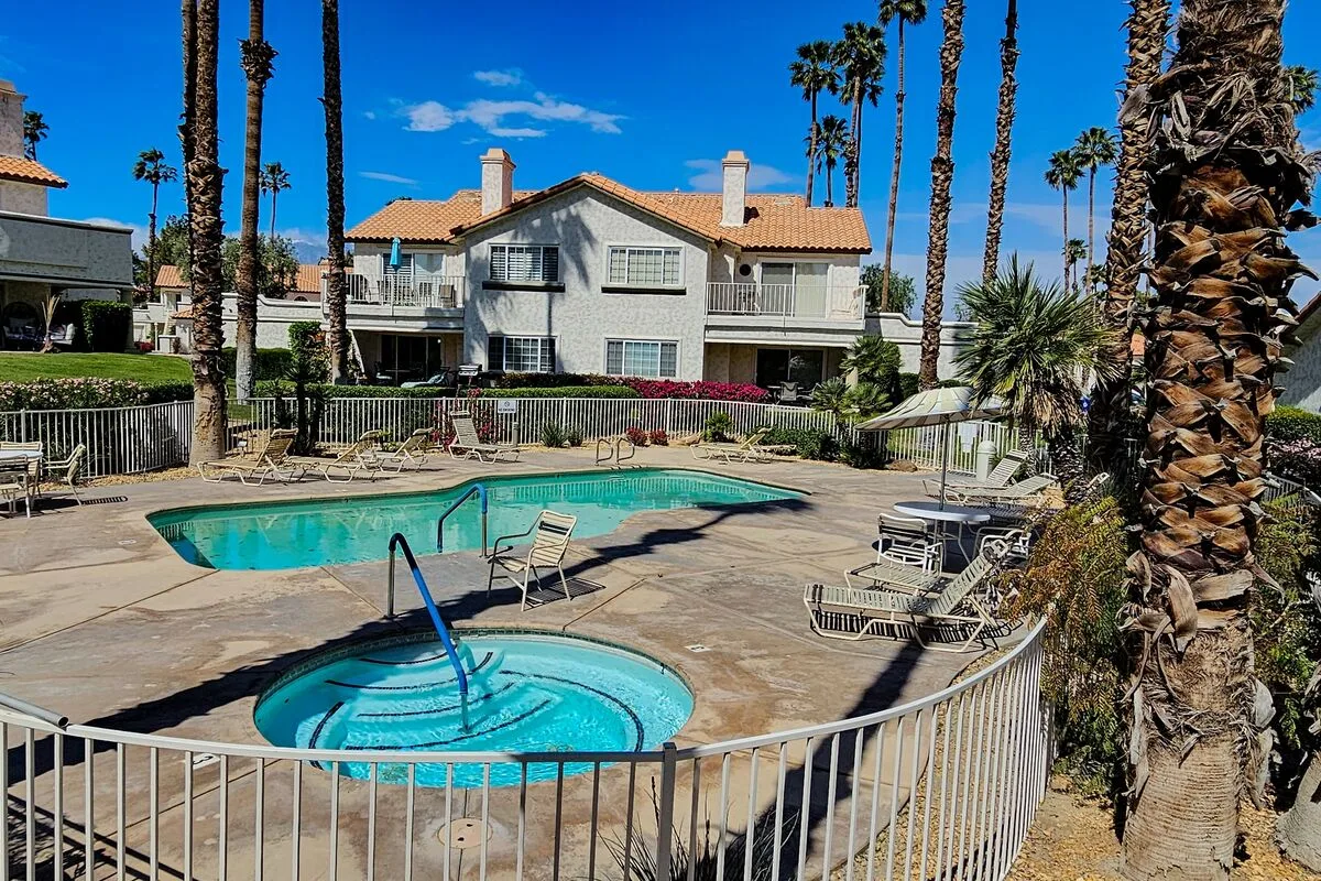 An outdoor pool and circular spa sit beside a paved deck and palm trees.