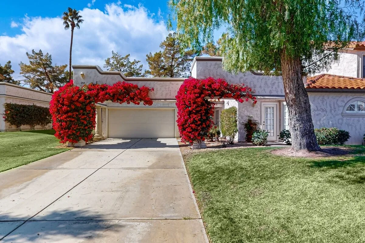 A house exterior with a driveway, lawn, and bright flowering vines.