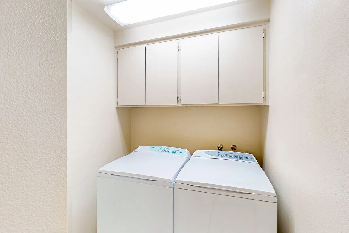 A laundry area with two white washing machines beneath overhead cabinets.