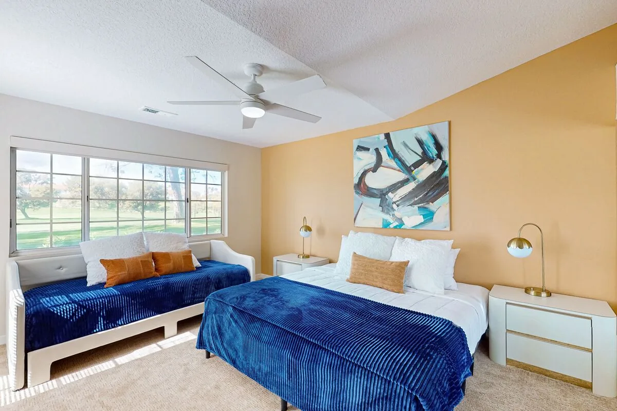 A bedroom with two beds dressed in blue bedding and a large window.