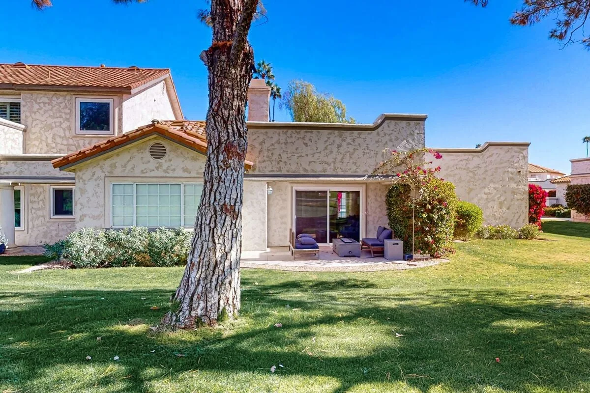 A landscaped yard with a large tree in front of a house and outdoor seating.