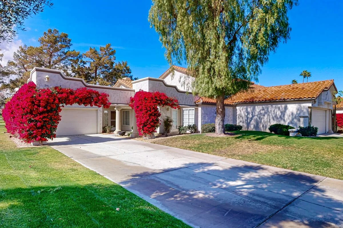 A white stucco house with a driveway, lawn, and flowering vines.