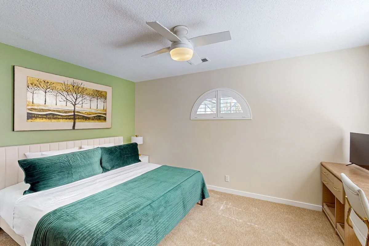A bedroom with a bed dressed in teal bedding and framed artwork on a green wall.